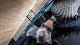 Person wearing safety equipment operates a power tool close to a wooden surface.