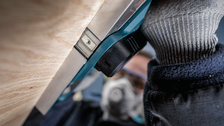 Person wearing safety equipment operates a power tool close to a wooden surface.