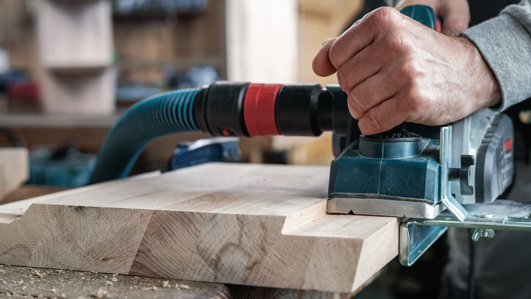 Person uses a power planer on a wooden board in a workshop.