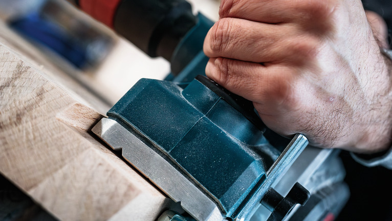Person uses a power tool to shape wood.