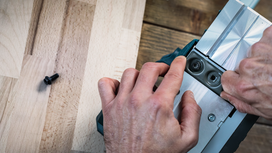 Person adjusting a metal power tool part on a wooden surface.