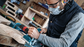 Person wearing safety equipment operates a power saw to cut wooden boards.