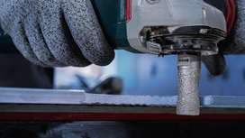 Person wearing safety equipment grinds the edge of a metal surface with a power tool.