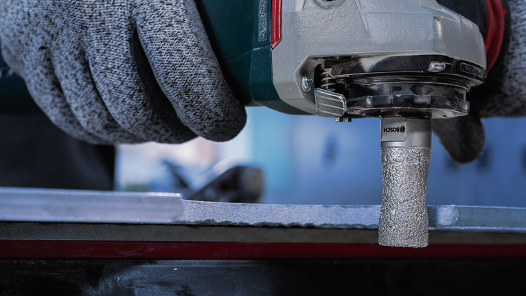 Person wearing safety equipment grinds the edge of a metal surface with a power tool.