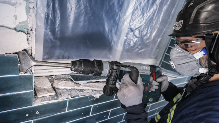 PRO SDS max-4C Tile Chisel, 80 x 300 mm Worker wearing safety equipment removes wall tiles using a demolition hammer.