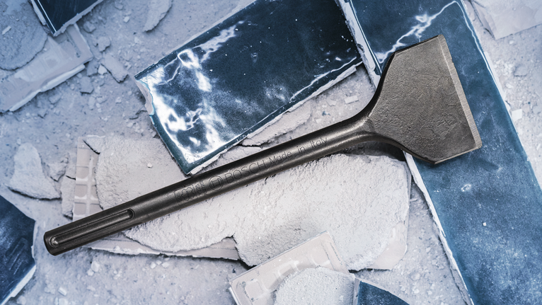 PRO SDS max-4C Tile Chisel, 80 x 300 mm Wide chisel rests on broken concrete slabs covered in dust.