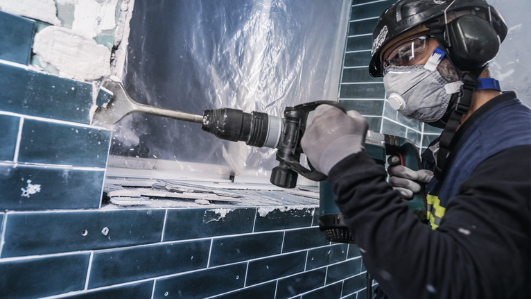 PRO SDS max-4C Tile Chisel, 80 x 300 mm A person wearing safety equipment removes tiles with a demolition hammer.