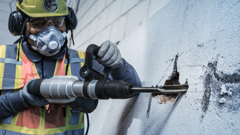 PRO SDS max Hollow Gouging Chisel, 26 x 300 mm A person wearing safety equipment uses a rotary hammer to break a hole in a concrete wall.