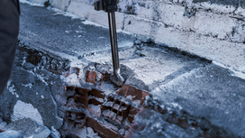 Demolition tool breaking concrete on a brick wall.