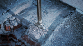Chisel breaking concrete, scattering dust and debris.