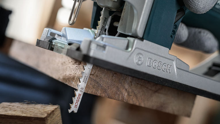 PRO Hardwood fast T144DF Jigsaw Blade, 100 mm, 5 pcs Person wearing safety equipment uses a jigsaw to cut a wooden board.