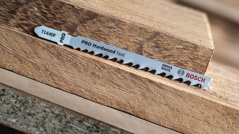 PRO Hardwood fast T144DF Jigsaw Blade, 100 mm, 5 pcs Jigsaw blade lying on stacked pieces of hardwood.