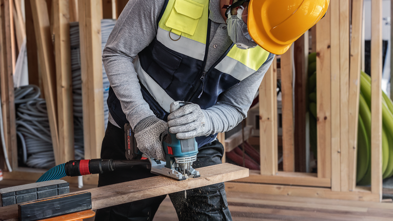 PRO Hardwood fast T144DF Jigsaw Blade, 100 mm, 5 pcs A person wearing safety equipment cuts wood with a power tool at a construction site.