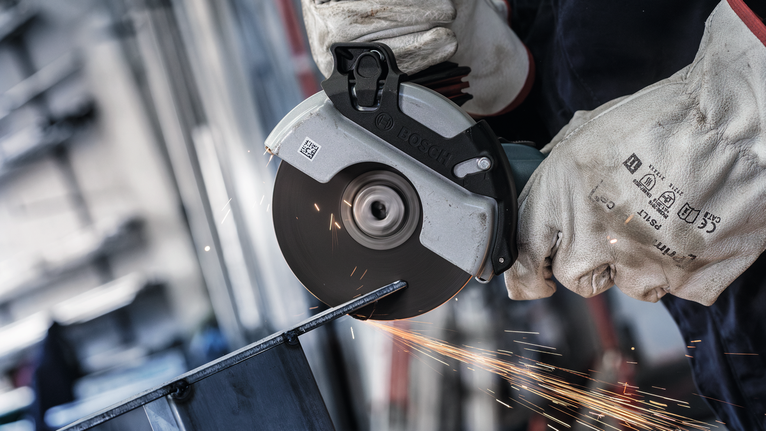 PRO Stainless Steel and Metal Bonded Cutting Disc, 125 x 1.6 x 22.23 mm, X-Lock, Straight, oSa Person wearing safety equipment uses an angle grinder to cut metal, producing sparks.