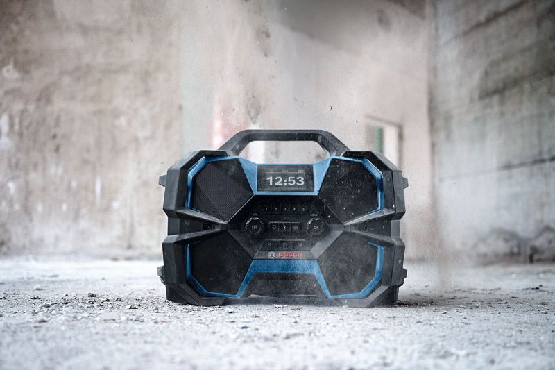 Rugged jobsite radio sitting on a dusty concrete floor in a partially finished building.