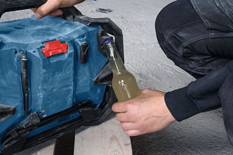 A person uses a portable jobsite radio to open a glass bottle on a construction site.