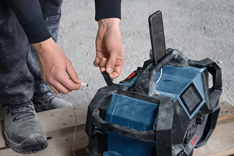 Person wearing safety equipment plugs a charging cable into a rugged jobsite radio.