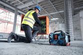 A person wearing safety equipment connects wires at a construction site near a jobsite radio.