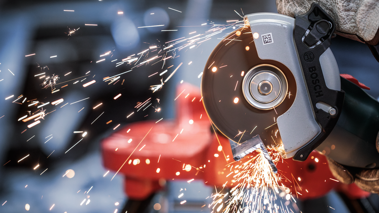 PRO Metal Bonded Cutting Disc, 125 x 2.5 x 22.23 mm, X-Lock, Straight A person wearing safety equipment uses an angle grinder to cut metal, producing sparks.