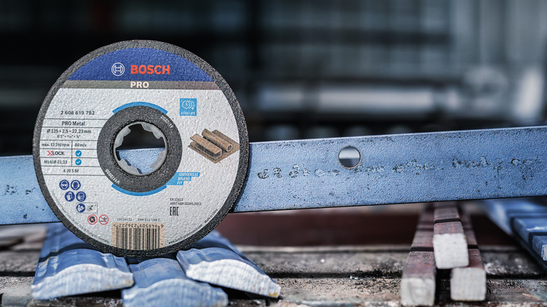 PRO Metal Bonded Cutting Disc, 125 x 2.5 x 22.23 mm, X-Lock, Straight Cutting disc placed upright next to a metal bar with a hole in a workshop.
