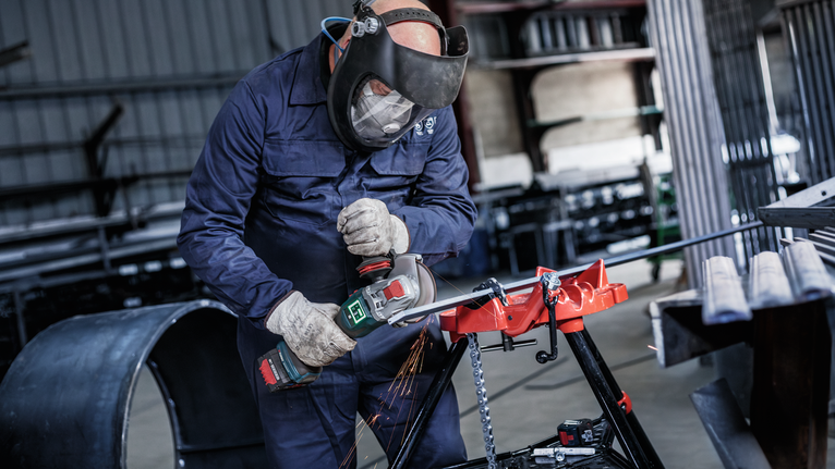 PRO Metal Bonded Cutting Disc, 125 x 2.5 x 22.23 mm, X-Lock, Straight A person wearing safety equipment uses an angle grinder to cut metal, producing sparks.