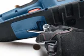 A person wearing safety equipment uses a hex wrench on a cordless chainsaw.