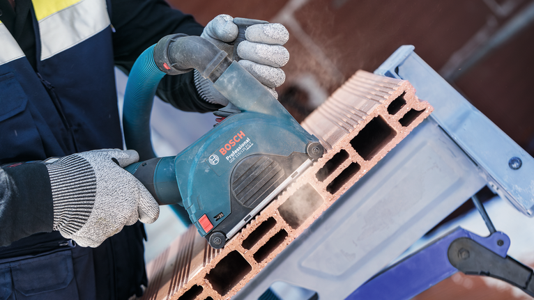 A person wearing safety equipment cuts a hollow brick with a power tool.