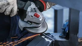 A person wearing safety equipment grinds metal, creating sparks.