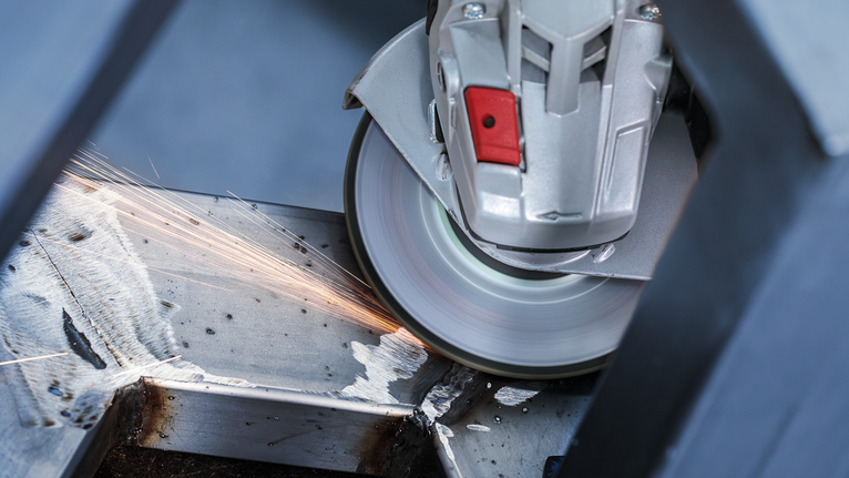 Angle grinder cutting through a metal beam, producing sparks.
