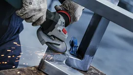A person wearing safety equipment grinds a metal frame, with sparks flying.