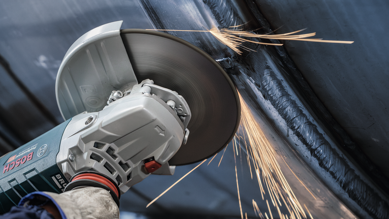A person wearing safety equipment grinds metal, producing sparks.
