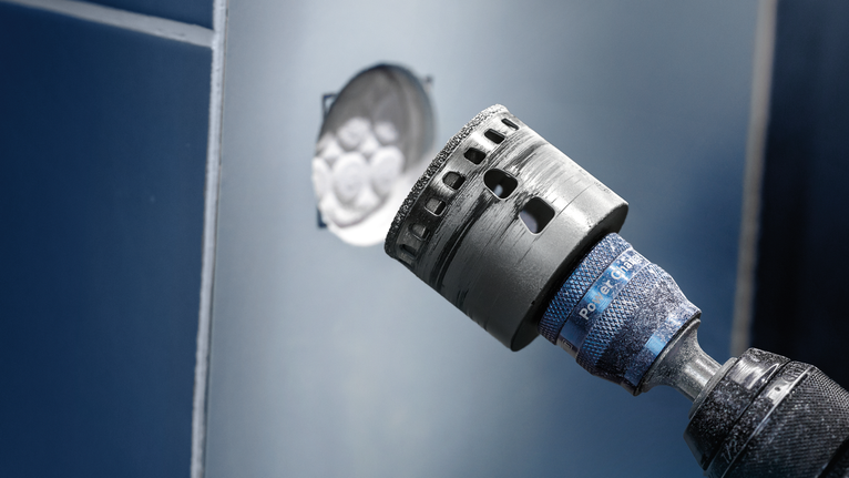 Hole saw attachment drilling a circular opening in a blue panel.