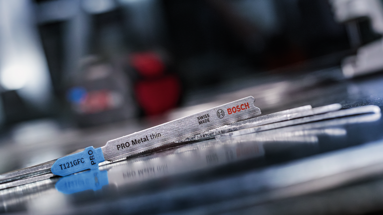 Metal jigsaw blades lying on a reflective metal surface in a workshop.