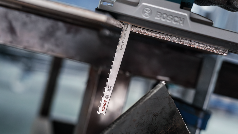 Person wearing safety equipment uses a jigsaw to cut through a metal sheet.