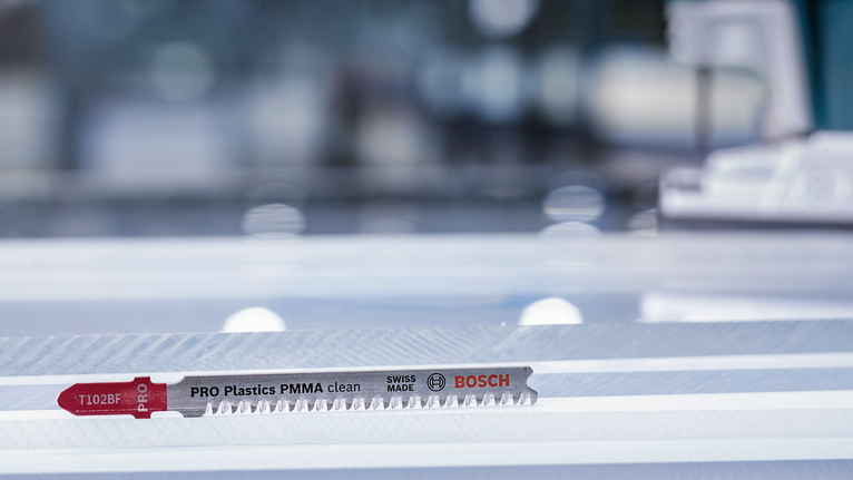 Jigsaw blade resting on a clear plastic sheet in a workshop setting.