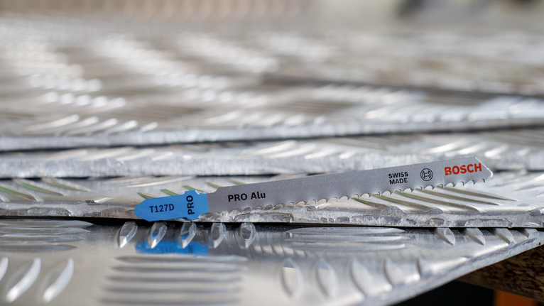 PRO Alu T127D Jigsaw Blade, 100 mm, 5 pcs Saw blade resting on stacked sheets of textured metal.