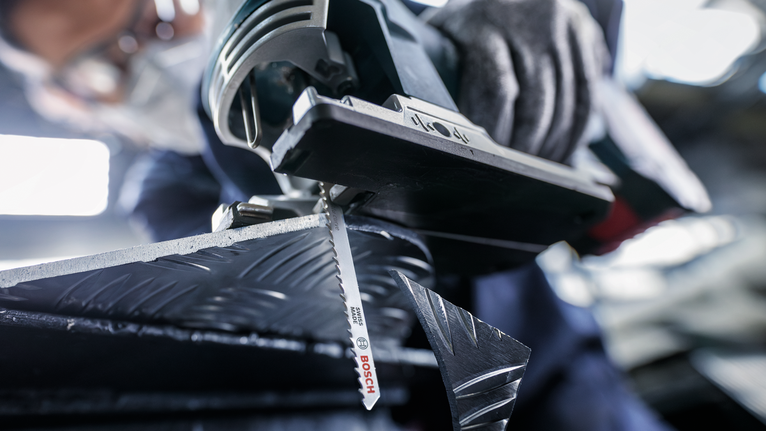 PRO Alu curve T227D Jigsaw Blade, 100 mm, 5 pcs A person wearing safety equipment cuts patterned metal with a jigsaw.