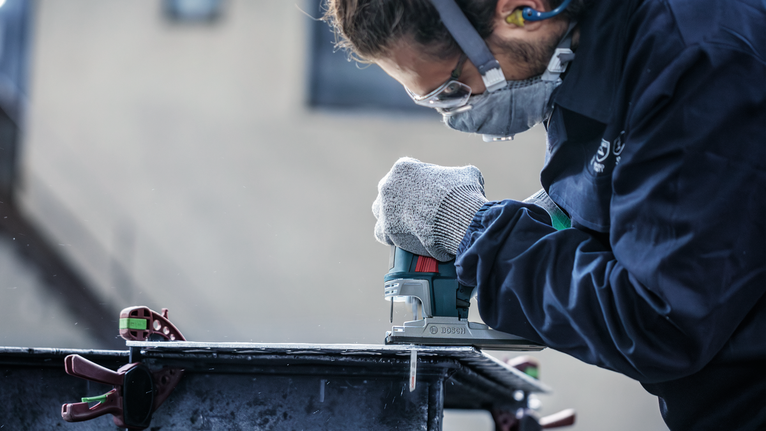 PRO Alu curve T227D Jigsaw Blade, 100 mm, 5 pcs Person wearing safety equipment uses a jigsaw to cut a metal sheet.