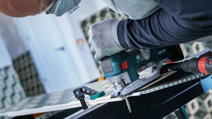 Object #200469110: 3066410_app_web_3 Person wearing safety equipment cuts tile with an electric jigsaw on a workbench.