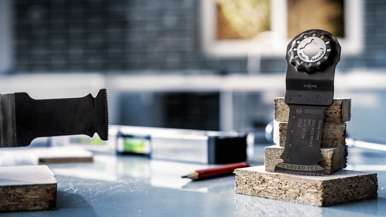 PRO AIZ 32 APIB Plunge Cut Blade, 32 x 50 mm Oscillating multi-tool blade and attachment resting on stacked wood pieces.