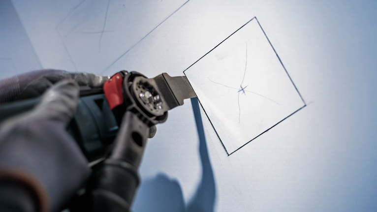 PRO AIZ 32 APIB Plunge Cut Blade, 32 x 50 mm Person wearing safety equipment uses a power tool to cut a square in drywall.