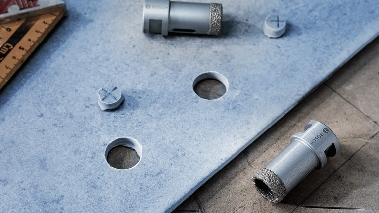 Diamond core drill bits and a ruler beside holes cut in a blue ceramic tile.