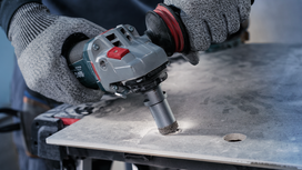 Person wearing safety equipment drills a hole into a large tile sheet.