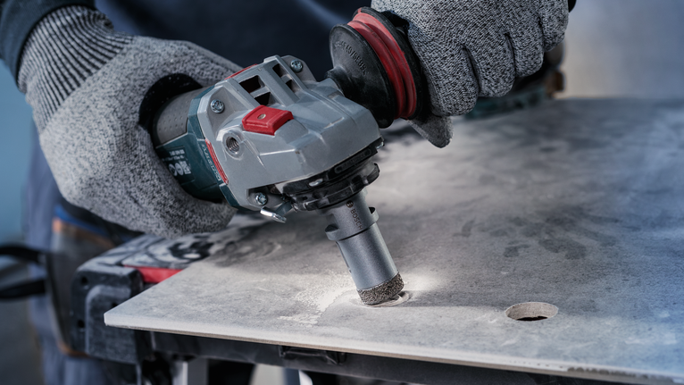 Person wearing safety equipment drills a hole into a large tile sheet.