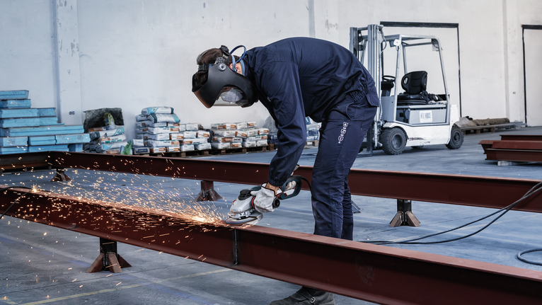 PRO Metal Grinding Disc, A 24 S BF, 180 x 6.6 x 22.23 mm, Depressed Centre A person wearing safety equipment grinds a metal beam, producing sparks in a warehouse.