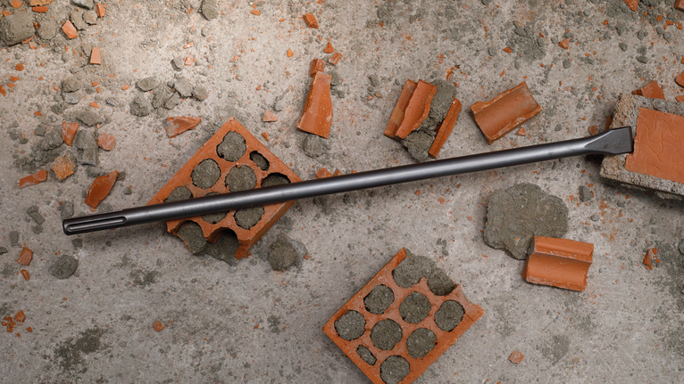 PRO SDS max-4C Flat Chisel, 25 x 600 mm Chisel bit lying on a concrete surface surrounded by broken bricks.