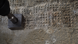 Metal tool making square indentations on rough concrete surface.