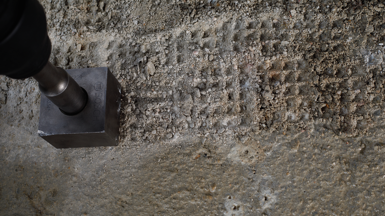 Metal tool making square indentations on rough concrete surface.