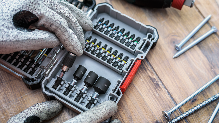 Person wearing safety equipment selects a screwdriver bit from an organized case.