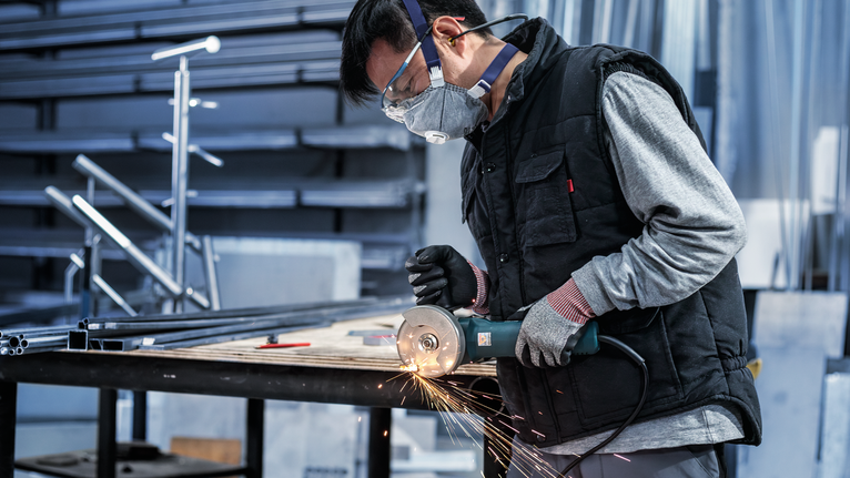 Person wearing safety equipment grinds metal, creating sparks in a workshop.